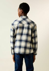 Kariertes Flanellhemd in Creme, Marineblau und Hellblau. Lange Ärmel, Knopfmanschetten und ein Rückenpasse. Legerer Schnitt.