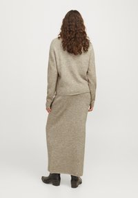 Beżowy dzianinowy sweter o luźnym kroju, zestawiony z pasującą maxi spódnicą. Stylizacja ma długie rękawy i prostą, gładką teksturę.