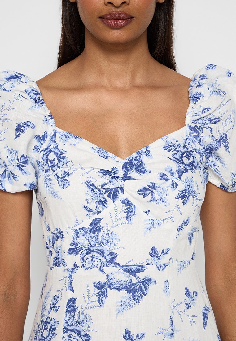 Weißes Kurzarmkleid mit blauem Blumenmuster, mit quadratischem Ausschnitt und gerafften Ärmeln. Weicher, strukturierter Stoff.