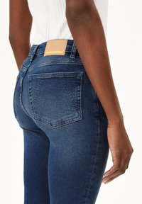 Jean taille haute bleu foncé en denim, avec une étiquette en cuir portant "ARMEDANGELS" sur la taille et deux poches au dos.