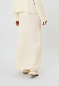 Pitkä, kermaisen värinen neulottu hame pehmeästä kankaasta, yhdistetty beigen värisiin urheilukenkiin, rento istuvuus ja hienovarainen tekstuuri.