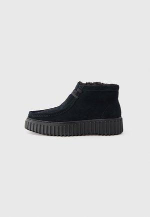 Chaussure basse en daim noir avec semelle épaisse en caoutchouc striée et lacets sur le devant, avec une doublure intérieure en peluche pour la chaleur.