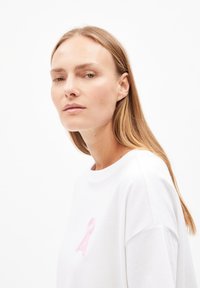 Witte katoenen T-shirt met een roze lint geborduurd op de linkerkant van de borst. Losse pasvorm met een ronde halslijn en korte mouwen.