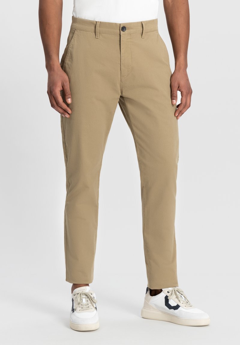 Bežīgi chinosar slim fit, izgatavoti no gludas kokvilnas auduma. Iespējams ar pogu aizdari un priekšējiem kabatām, apvienoti ar baltām tenisa kedām.