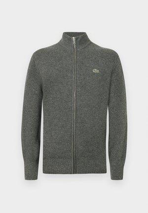 Sivý kardigán na zips z pletenej vlny. Má rebrovaný golier, manžety a lem, s malým zeleným logom na prsiach.