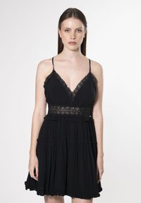 Schwarzes Kleid mit Spaghetti-Trägern, einem mit Spitze verzierten Ausschnitt, gestuften Rüschen und einer taillierten Spitze. Glatte Stoffoberfläche.