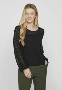 Mustmust läheb mustast heegeldatud kampsunist, millel on pikad varrukad, ümar kaelus ja tekstuuriga muster. Ühendatud oliivroheliste pükste ehk pükste paariga.