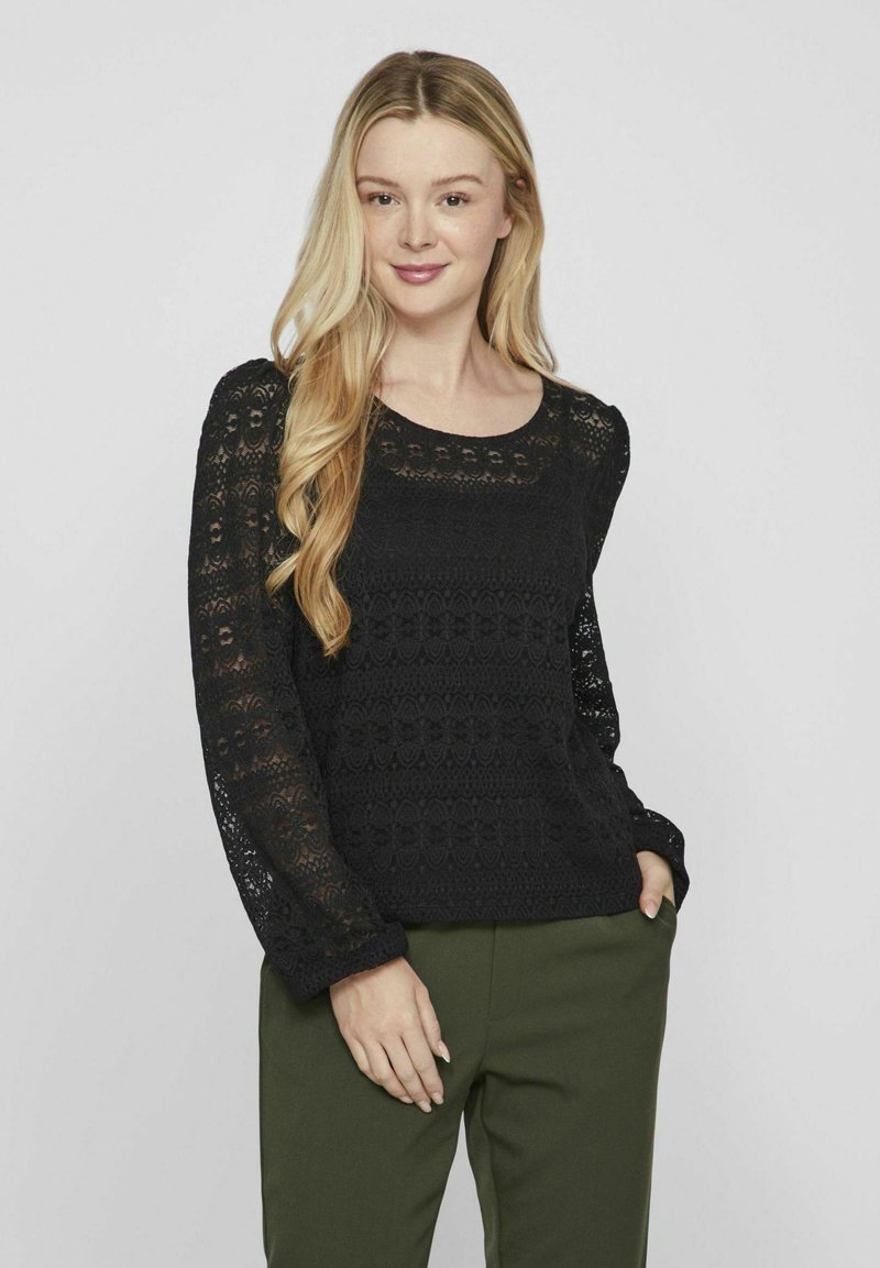 Mustmust läheb mustast heegeldatud kampsunist, millel on pikad varrukad, ümar kaelus ja tekstuuriga muster. Ühendatud oliivroheliste pükste ehk pükste paariga.