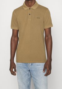 Olivgrön polo med två knappar, korta ärmar och subtil logotypdetaljering. Tillverkad av ett mjukt och smidigt bomullsmaterial.