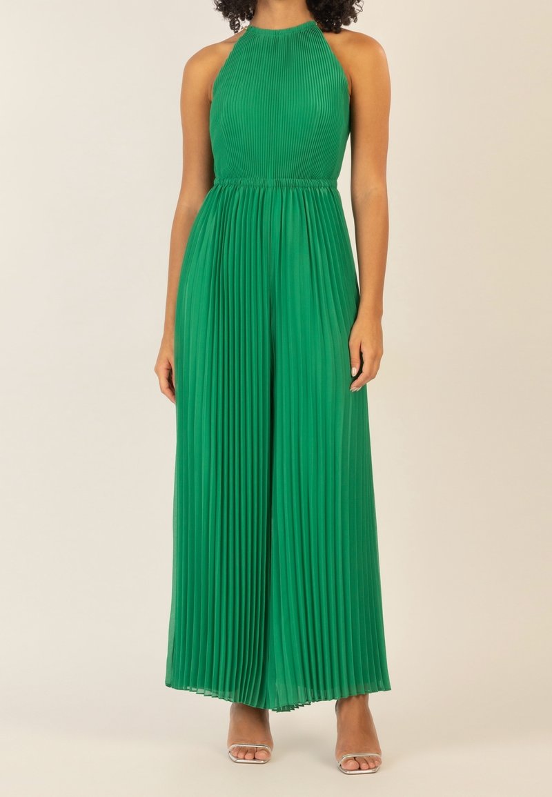 Green pleated jumpsuit with a halter neck design, flowing wide legs, and a textured fabric. Silver strap sandals complete the look.
