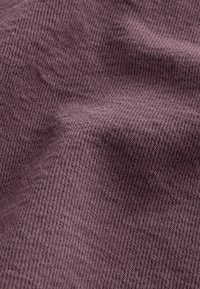 Mörklila tyg med en fin, texturerad väv; materialet verkar mjukt med en subtil lyster och en lätt sträckning, som visar upp intrikata detaljer.