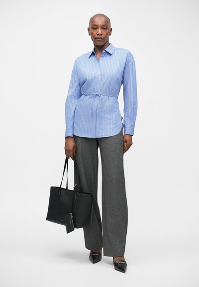 Blauw-witte gestreepte button-up shirt met een strakke taille, gecombineerd met grijze wijde broek. Een zwarte tote bag maakt de outfit compleet.