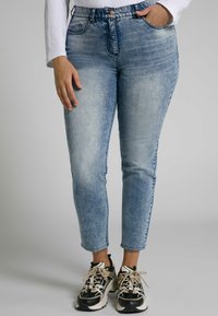 Ljust blå högmidjade jeans med en urtvättad look, med fem fickor, bältesöglor och en slitna kant. Kombineras med kraftiga svarta sneakers.