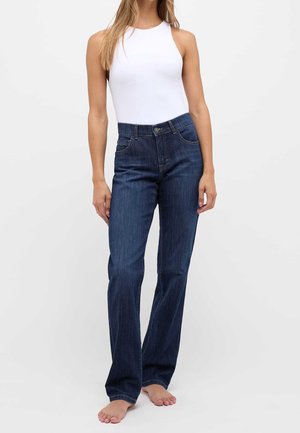 Jeans blu scuro con taglio dritto, tasche frontali e cintura. Abbinati a un body senza maniche bianco. Scarpe non visibili.