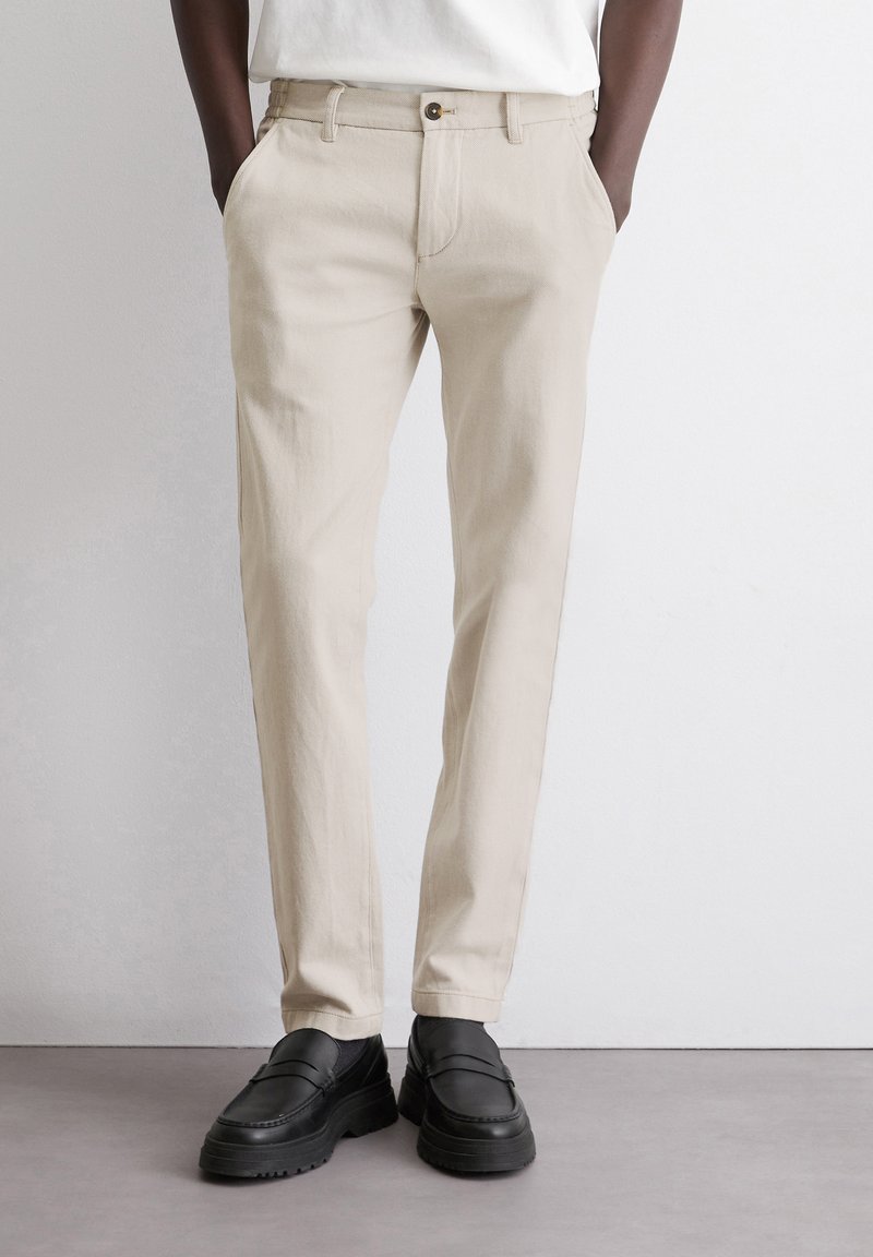 Beige broek met een slanke pasvorm en recht model, voorzien van een sluiting met een knoop aan de voorkant en zijzakken. Draag het met zwarte schoenen.
