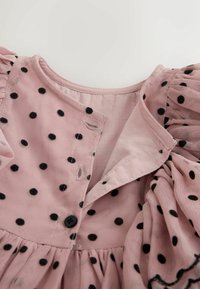 Tela rosa con lunares negros, con una manga abullonada fruncida y un escote con botones y ojales visibles.