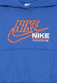 Plava dukserica s kapuljačom s velikim, reljefnim narančastim Nike logotipom koji prikazuje efekt munje, bijelim tekstom "Nike Sportswear" i džepom za kengure.