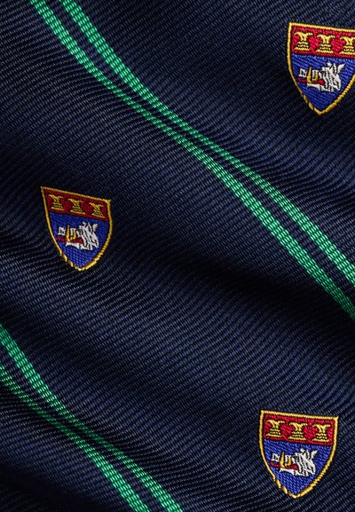 Ύφασμα σκούρου μπλε με πράσινες διαγώνιες ρίγες, με κεντημένες ασπίδες που έχουν κόκκινο πάνω μέρος, μπλε κάτω μέρος και λευκό ζώο που κρατάει έναν σωλήνα.