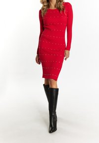 Robe rouge côtelée à manches longues, ornée de clous argentés. Portée avec des bottes en cuir noires jusqu'aux genoux, de forme ajustée et avec une fente sur le côté.