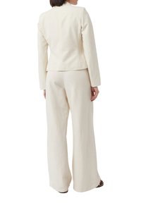 Beżowa lniana marynarka z dopasowanymi szerokimi spodniami, wyróżniająca się dopasowanym krojem, gładką fakturą i minimalistycznym designem.