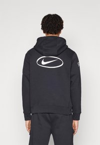 Svart Nike hoodie med en stor vit logotyp på baksidan. Har en rymlig huva, ribbade manschetter och en ribbad nederkant, tillverkad av mjukt bomullsblandat material.