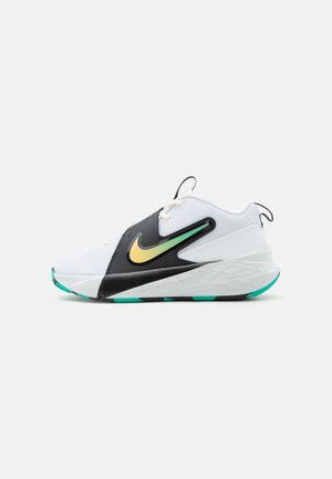 Chaussure de sport blanche avec un swoosh Nike noir et jaune-vert, dessus en mesh, semelle épaisse blanche, et accents bleu sarcelle sur les bords de la semelle.