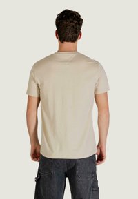 Beige kurzärmeliges T-Shirt aus weichem Stoff, mit klassischem Rundhalsausschnitt und lockerem Schnitt, getragen mit dunkelgrauen Cargo-Hosen.