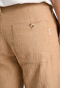 Ljusbruna herringbone byxor har en bakficka med knappstängning och en liten varumärkesetikett på midjan.