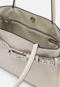 Beżowa skórzana torba na ramię z srebrnym okuciem, z dekoracyjnym paskiem z okrągłymi akcentami i zasuwaną kieszenią w środku.