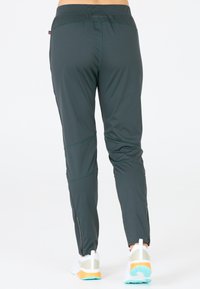 Donkergroene sportbroek met een aansluitend ontwerp, voorzien van ritssluitingen bij de enkels en contrasterende stiksels. Gemaakt van een gladde, ademende stof.