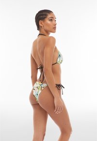 Bikini dengan pola bunga berwarna hijau dan kuning, dilengkapi dengan tali belakang hitam. Atasannya memiliki bentuk segitiga dengan desain minimalis.