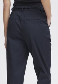 Pantaloni navy su misura con vita intrecciata, dotati di tasca posteriore e texture liscia, progettati per una vestibilità pulita e moderna.