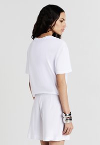 T-shirt en coton blanc à manches courtes, associé à un short blanc. Le modèle porte des bracelets en argent au poignet. Texture lisse et coupe décontractée.