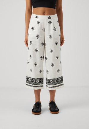 Witte wijde cropped broek met zwarte geometrische en bloemenpatronen, gedragen met zwarte sneakers en een zwart cropped topje.