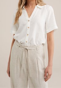 Vitt linne skjorta med krage, korta ärmar och guldknappar, parat med beige randiga högmidjade byxor och ett knutet bälte.