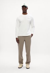 Bílá košile s dlouhými rukávy a logem na hrudi, béžové kalhoty a krémová kšiltovka se zeleným logem, doplněná světlými botami s designem tváře.