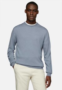 Light blue ribbed sweater with a crew neckline, long sleeves, and a subtle texture, paired with cream-colored trousers.