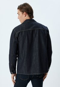 Dark denim jacket with a pointed collar, single back yoke, and contrasting stitching. Features button cuffs and straight cut design.