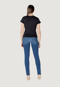 Zwarte katoenen t-shirt met korte mouwen, gecombineerd met blauwe skinny jeans. De jeans hebben een gemiddelde taille en achterzakken.