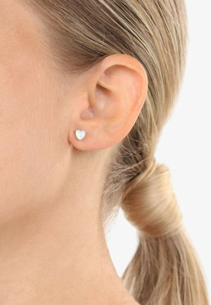 Orecchini a bottone a forma di cuore in argento con una finitura iridescente, posizionati sull'orecchio di un modello, che mostrano dettagli e design.