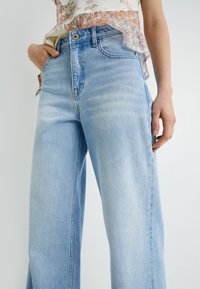 Jeans de pierna ancha de color azul claro, hechos de denim, con una cintura alta, un ligero desgaste y un diseño clásico de cinco bolsillos con cierre de botón metálico.