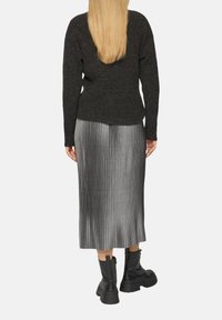 Zwarte gebreide sweater, zilveren geplooide midi-rok met hoge taille en zwarte chunky enkellaarsjes. De plooien lopen verticaal langs de rok.