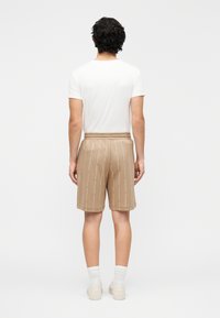 Smėlio spalvos šortai su vertikaliu pasikartojančiu raštu, elastinga juosmens juosta ir šoninėmis kišenėmis, priderinti prie paprasto balto marškinėlio ir baltų kojinių.