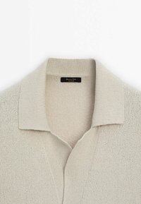 Beige gebreide polo trui met een geribbelde kraag en textuurstof. V-hals ontwerp met een label binnenin de kraag.