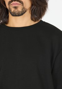 Mustan puuvillateepaita, jossa on pyöreä kaula-aukko ja rento istuvuus. Kankaan pinta näyttää pehmeältä, sillä on sileä rakenne eikä siinä ole näkyviä kuvioita tai korostuksia.