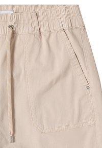 Short beige avec taille élastique, cordon de serrage et poche latérale en biais avec couture visible et petit rivet métallique.