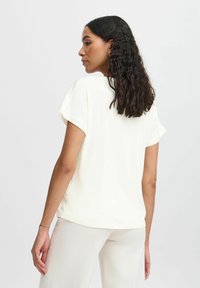 Kortärmad, lätt krämfärgad t-shirt med avslappnad passform, rund halsringning och något rundad nederkant. Slät textur.
