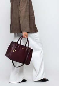 Person wearing white wide-leg pants, brown suede jacket, black shoes, holding a large dark purple leather handbag with gold details.