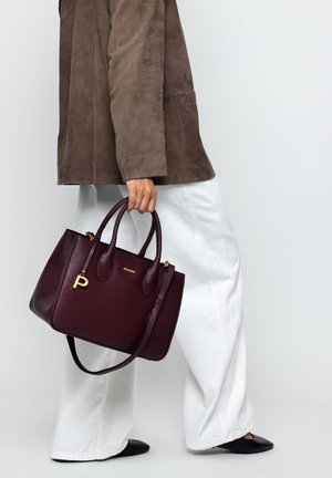 Person wearing white wide-leg pants, brown suede jacket, black shoes, holding a large dark purple leather handbag with gold details.
