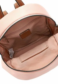 Rosa Stoff-Rucksackinnenseite mit einer einzelnen Reißverschlusstasche und einem kleinen braunen Etikett. Prüft braune Lederträger und einen schwarzen Reißverschluss.